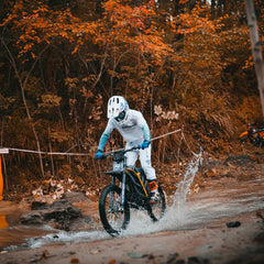 Biker crossing a stream on a 79BIKE-Falcon Pro Electric Dirt Bike in a forest setting