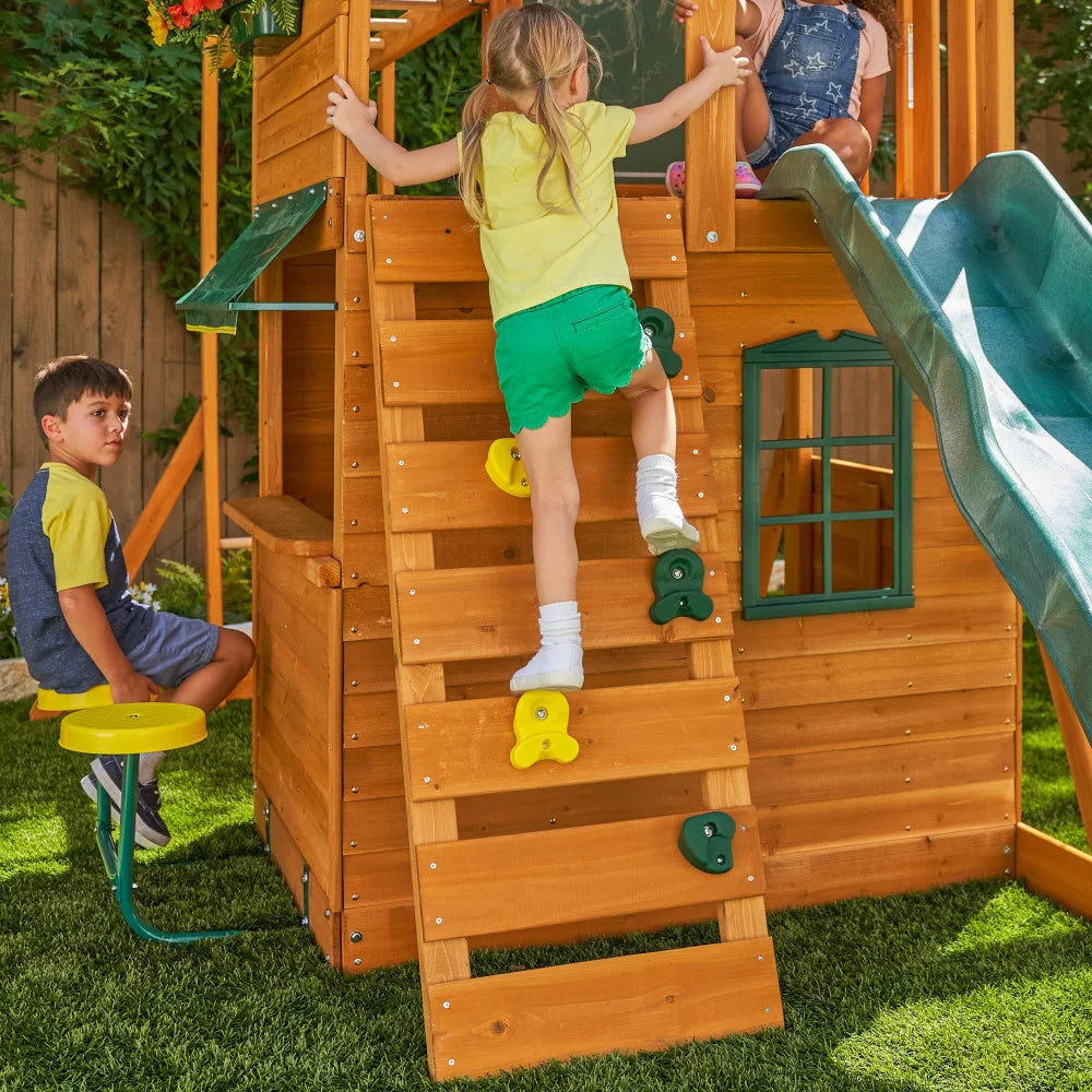 KidKraft Ridgeview Deluxe Clubhouse Children playing on a wooden playset with a slide in a backyard setting.
