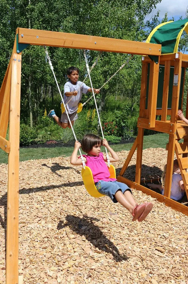Kidkraft Ainsley Outdoor Playset Children playing on a swing set in a playground.