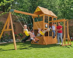 Kidkraft Overland Heights  Children playing on a wooden swing set with a playhouse in a backyard.