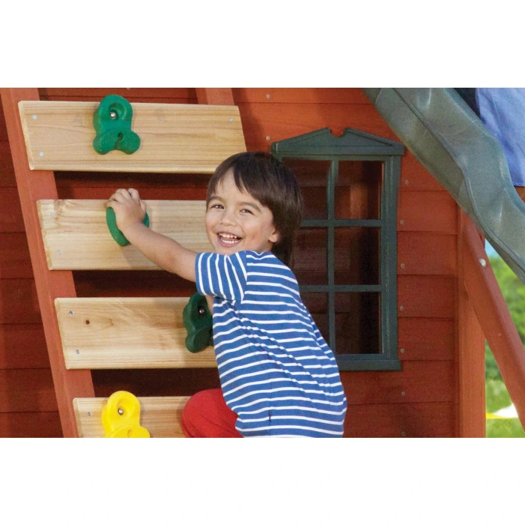 KidKraft Ridgeview Deluxe Clubhouse Child climbing a wooden ladder on a playhouse with a slide