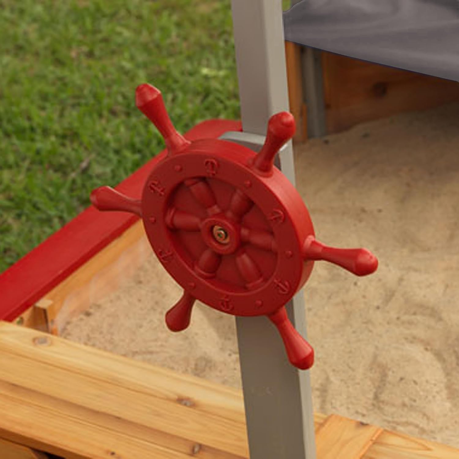 Red ship's pirate  wheel on a playground structure with grass and sand