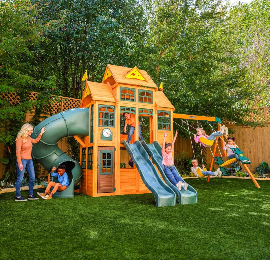 KidKraft Falcon Ridge Wooden Swing Set and Playset with Kitchen Children playing on a wooden playset with slides and swings in a backyard setting.