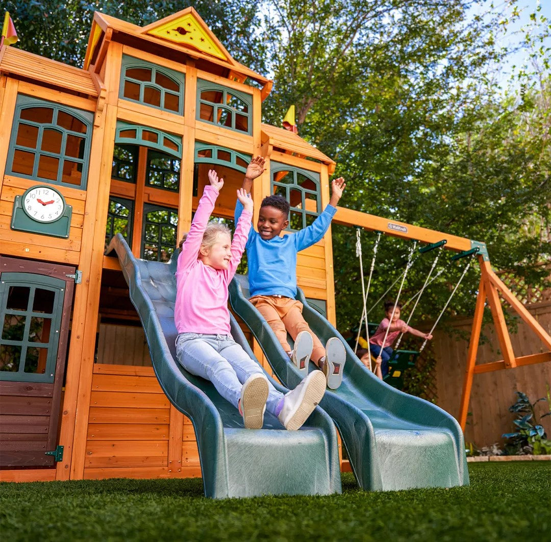 Children sliding down a slide on a wooden playset with a KidKraft Falcon Ridge Wooden