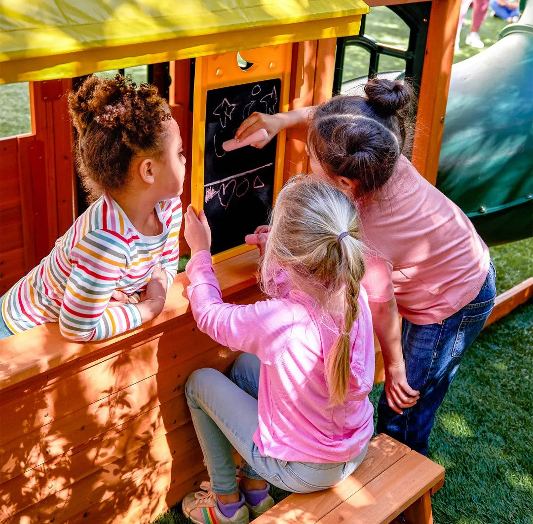 Children playing with a blackboard on a KidKraft Falcon Ridge Wooden playhouse