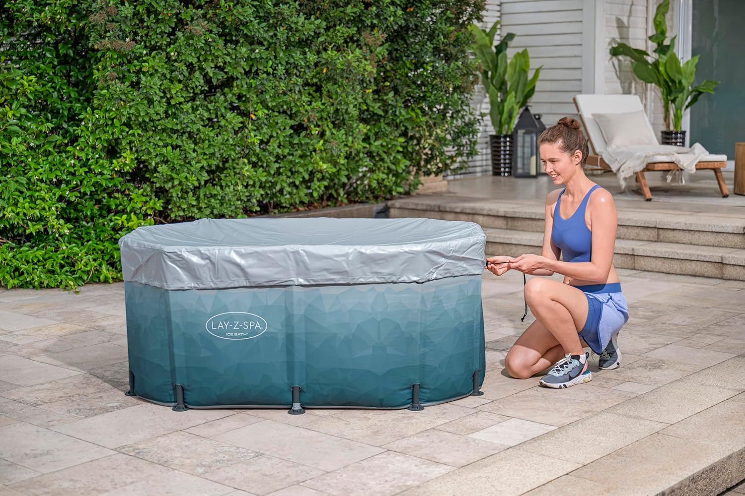 A woman is setting up an inflatable Ice tub outdoors on a patio.