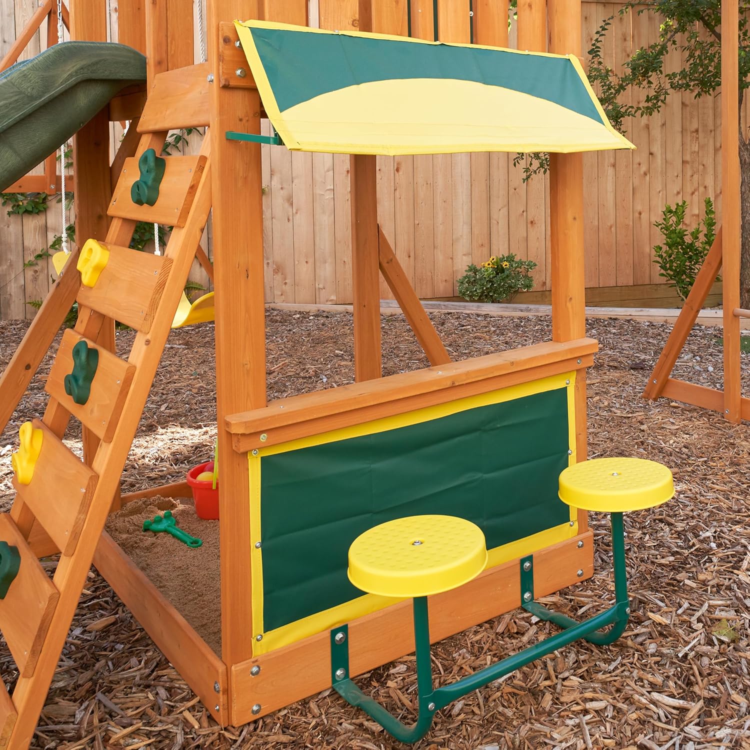 Kidkraft Brightside wooden playset with slide, climbing wall, and sand area in a backyard.