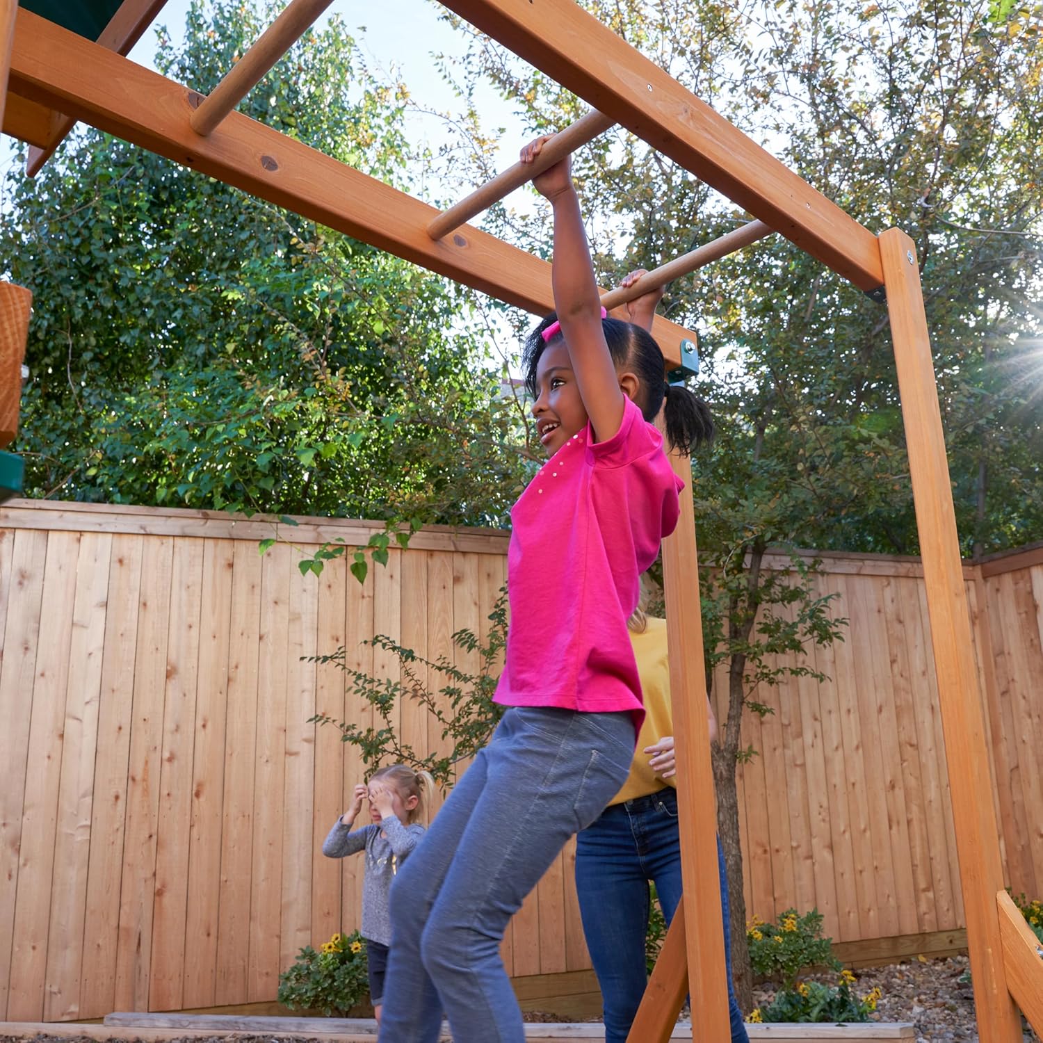 Kidkraft Brightside Child playing on a wooden playground structure with trees and a fence.