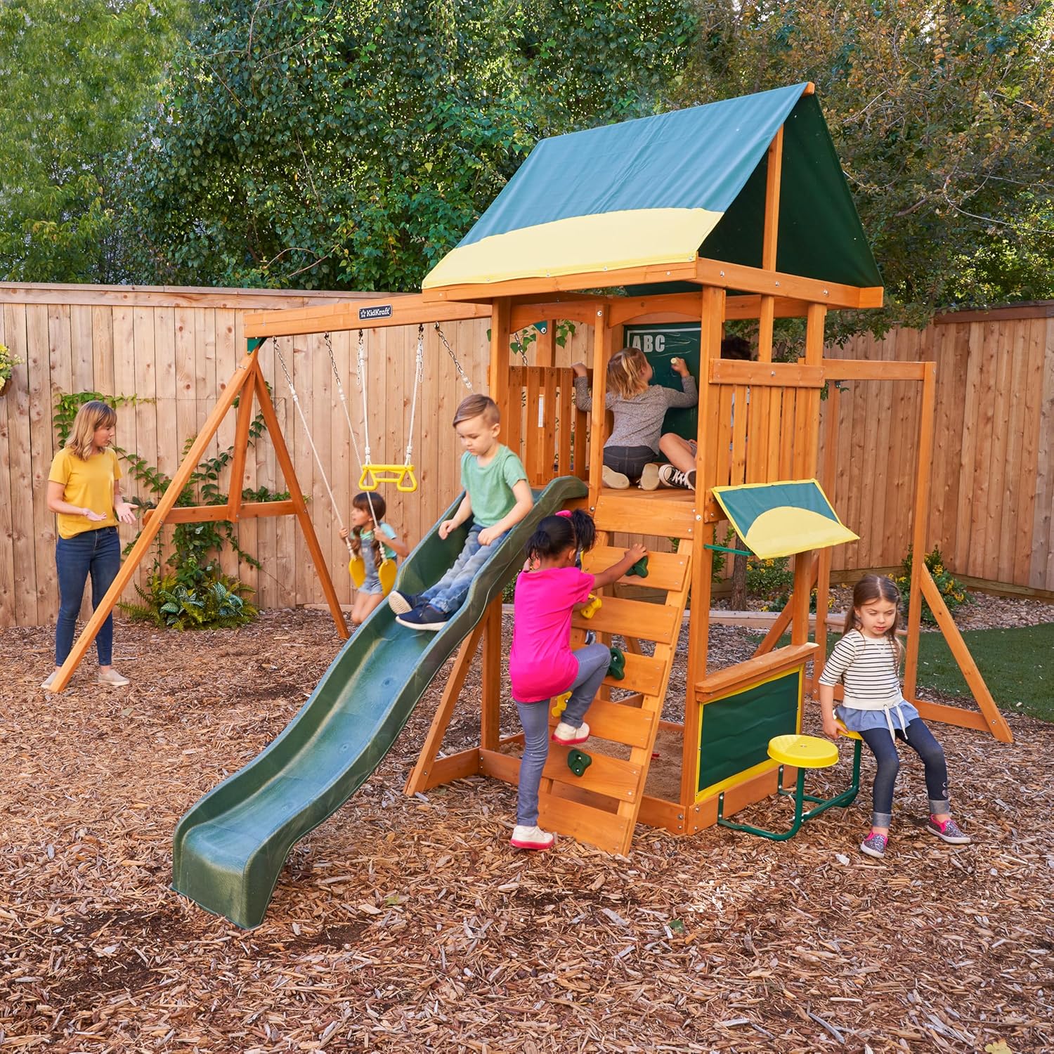 Kidkraft Brightside Children playing on a wooden playset with a slide in a backyard setting.