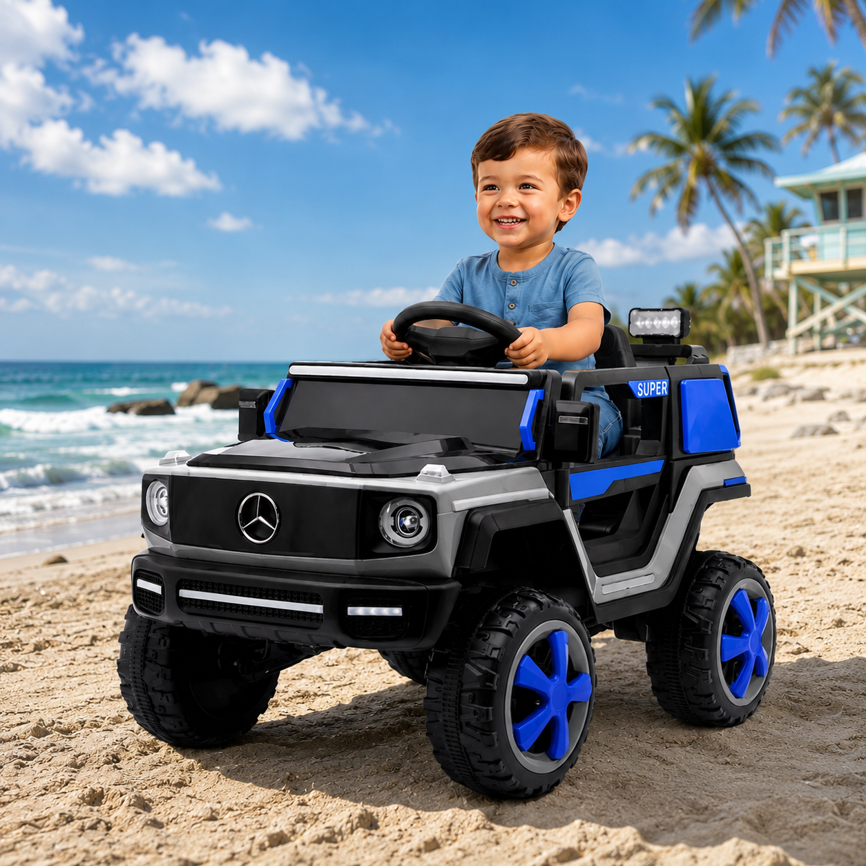 A young boy driving a black and blue Mercedes-Benz-style ride-on toy car on a sandy beach