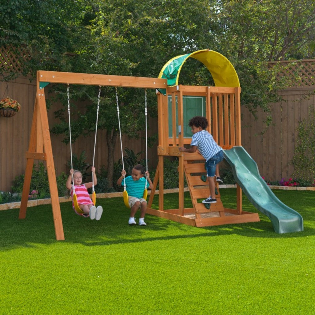 Kidkraft Ainsley Outdoor Playset Children playing on a wooden swing set with a slide in a backyard setting.