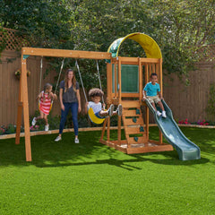 Kidkraft Ainsley Outdoor Playset Children playing on a wooden swing set with a slide in a backyard setting.