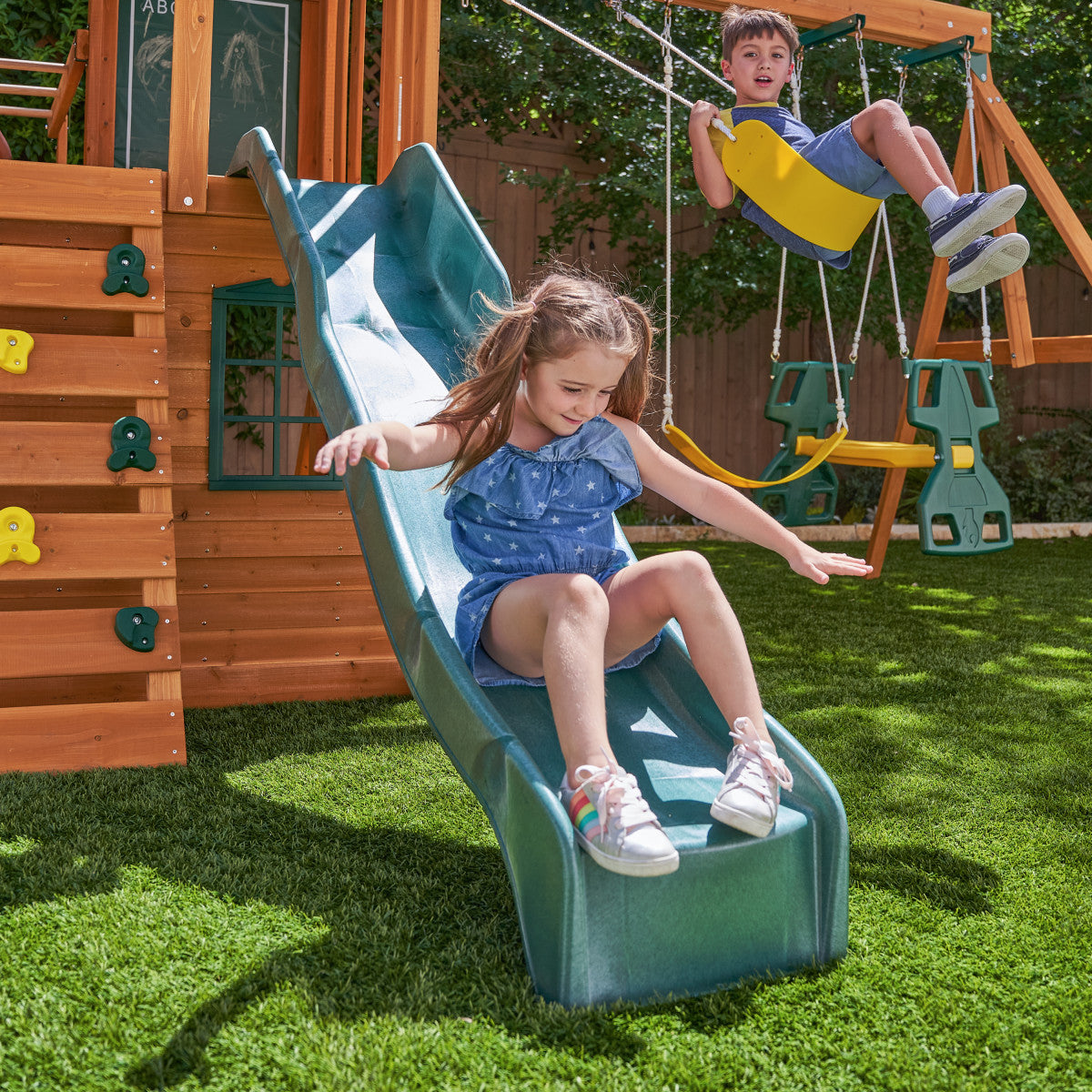 KidKraft Ridgeview Deluxe Clubhouse Children playing on a playground set with a slide and swings.