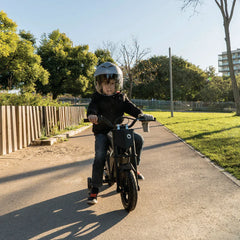 Child riding a small motorcycle on a path with trees and buildings