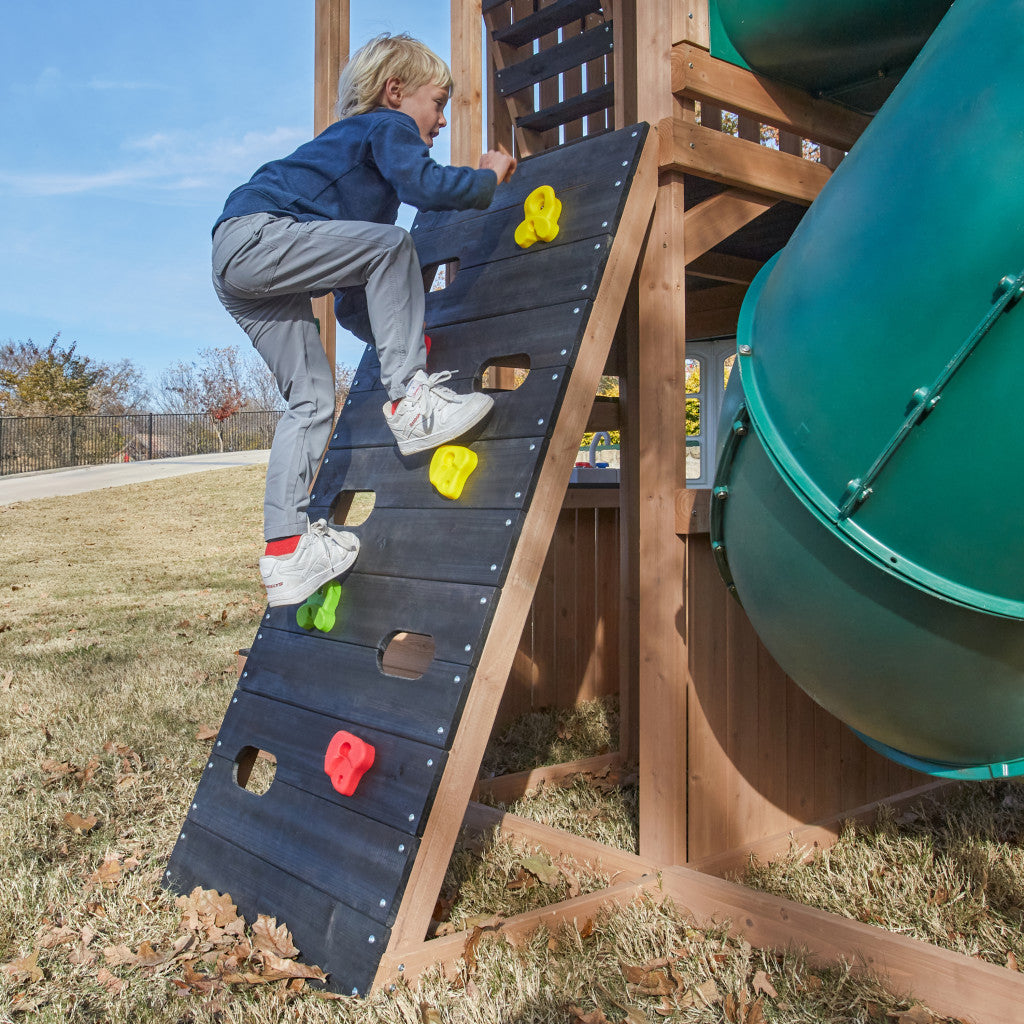Child climbing a wall climber  playground structure with a green slide on a sunny day.