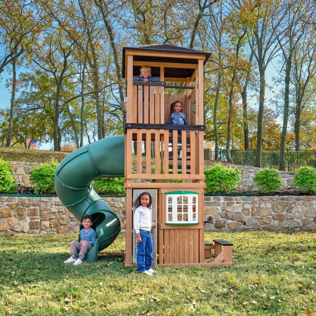 Children playing on a wooden playhouse with a green slide in a park with a terrace setting setting.