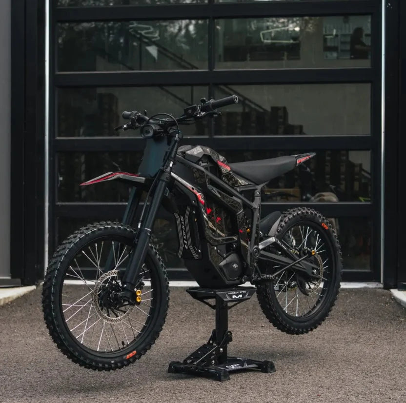 A black Talaria Sting MX5 Desert Beast 72V Electric Dirt Bike on a black stand