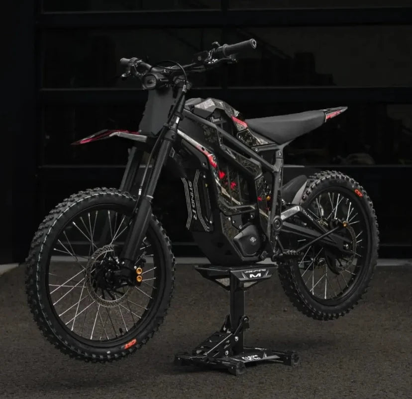 A black Talaria Sting MX5 Desert Beast 72V Electric Dirt Bike on a black stand