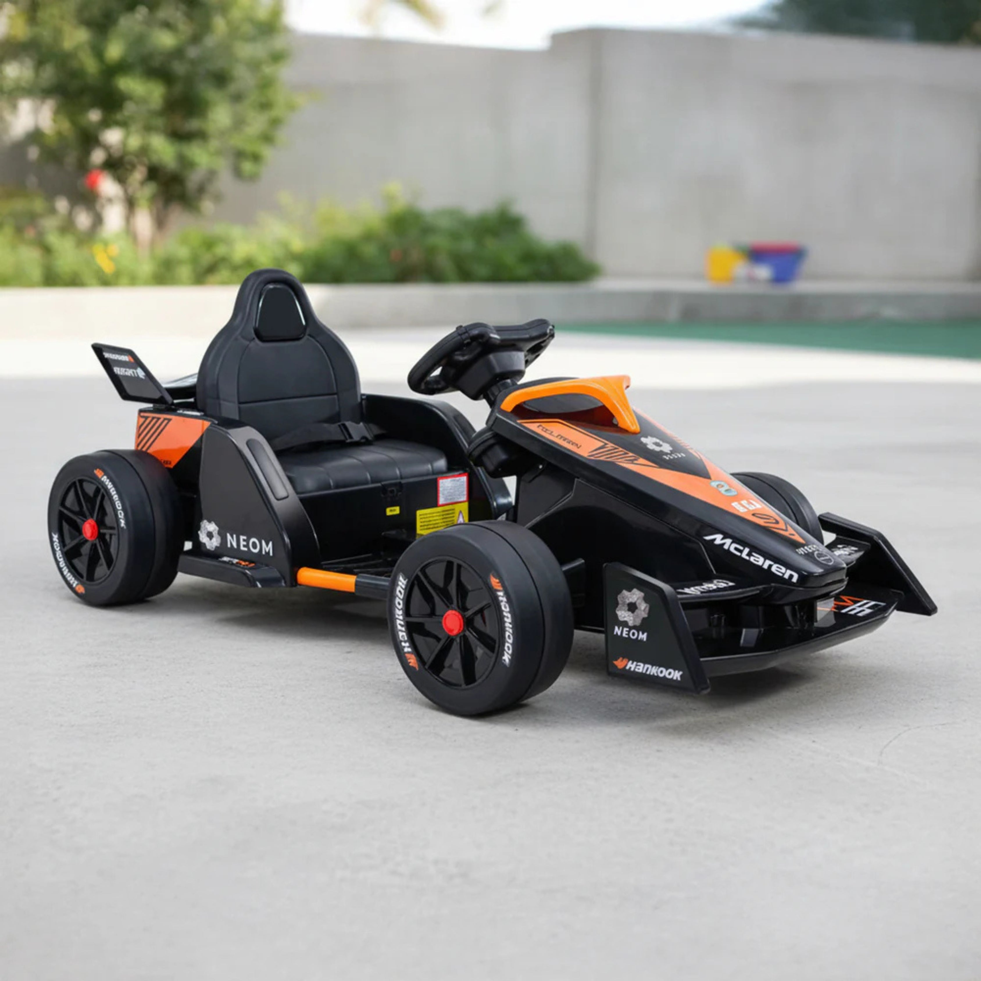 Black and orange go-kart on a concrete surface with greenery 