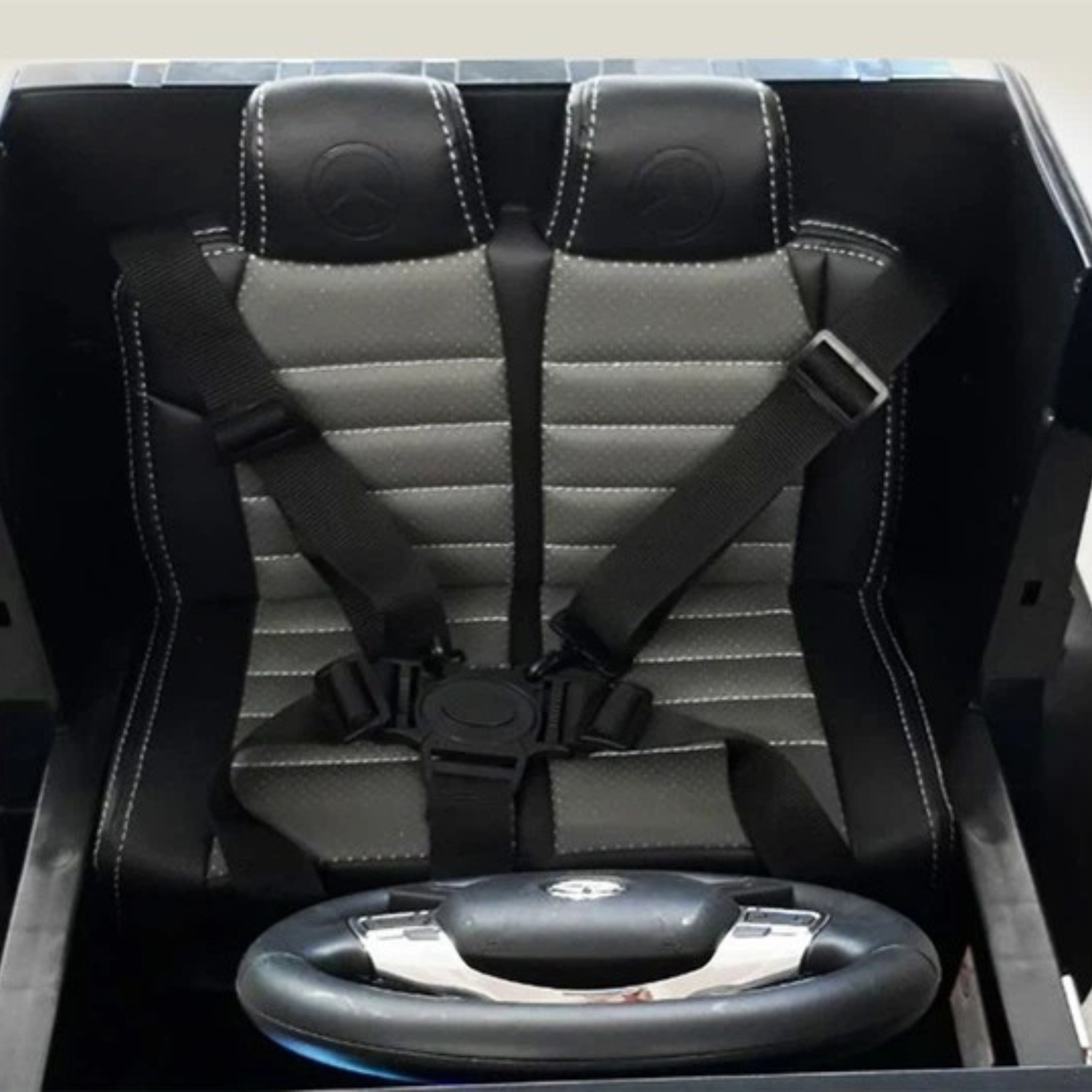 Black and grey car seat with safety harnesses and a steering wheel