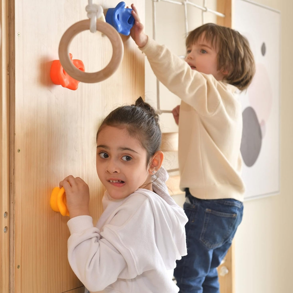 Two children climbing an indoor wooden climbing wall with colorful rock holds