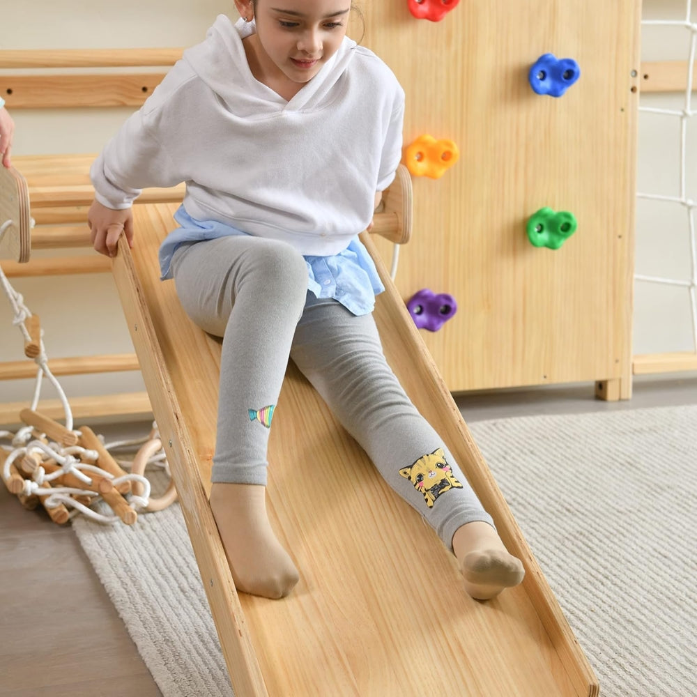 Child sliding down a wooden slide in a playroom with colourful climbing toys