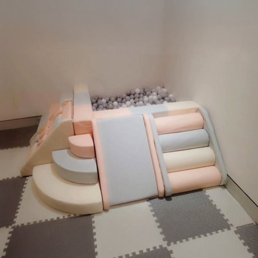 Pastel foam play set with soft slide, steps, and ball pit in an indoor playroom