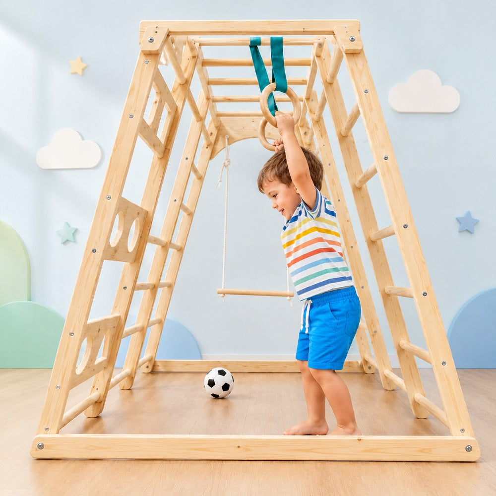 Child playing on a wooden climbing frame with rings in a room.