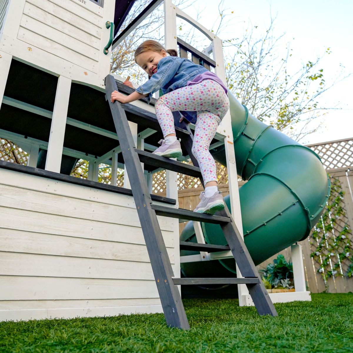 Kidkraft Wrangler Child climbing a ladder on a playhouse with a green slide