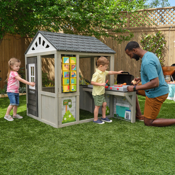 Children playing with a toy kitchen set in front of a playhouse