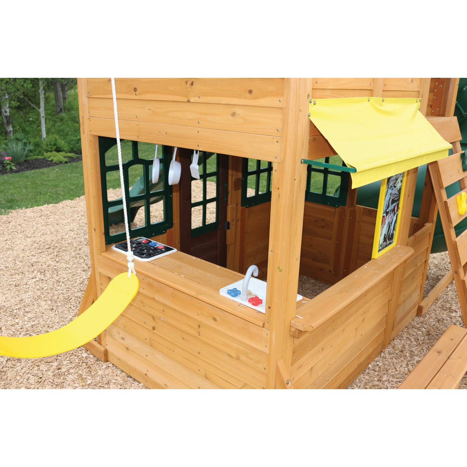 KidKraft Charleston Lodge Fort Wooden playhouse with yellow slide and kitchen accessories on a playground.