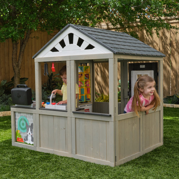 Children playing inside a wooden playhouse with the KidKraft Patio Party Playhouse