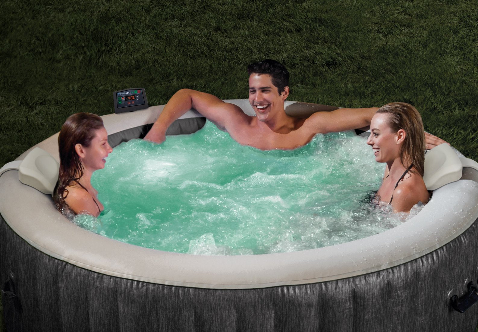 Three people in a hot tub with green water, surrounded by grass