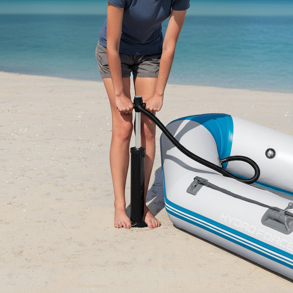 A person on a sandy beach using a manual black pump to inflate an inflatable boat.
