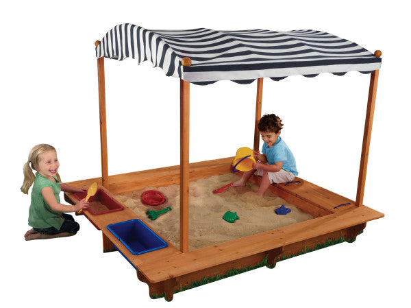 Children playing in a KidKraft Outdoor Covered Wooden Sandbox with a striped canopy