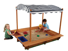 Children playing in a KidKraft Outdoor Covered Wooden Sandbox with a striped canopy