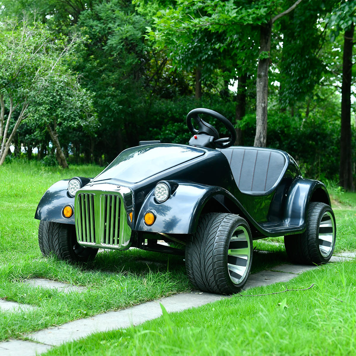 A black classic convertible off road 150 cc Fuel car is parked on a concrete path in a grassy park.