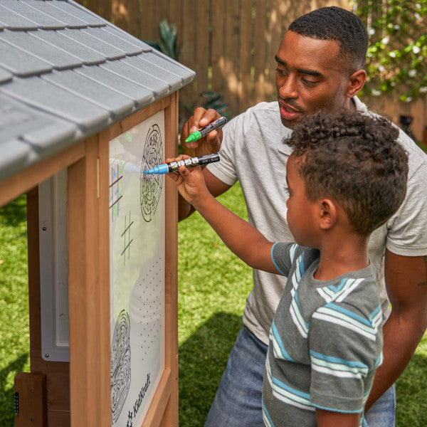 A man and a child are drawing white board on a wooden playhouse