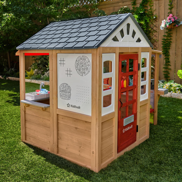 Wooden playhouse with a red door and grey roof, with white board