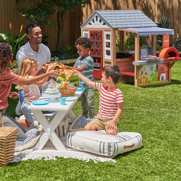A Family and children are enjoying a picnic with a playhouse.