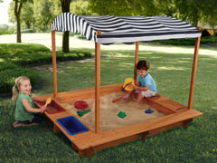 Children playing in a sandbox with a striped canopy on a grassy playhouse.